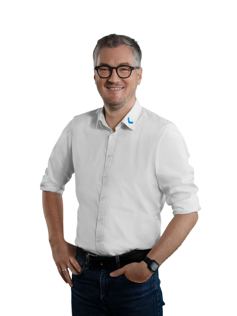 Mann mit Brille in weißem Hemd und blauer Jeans lächelt.