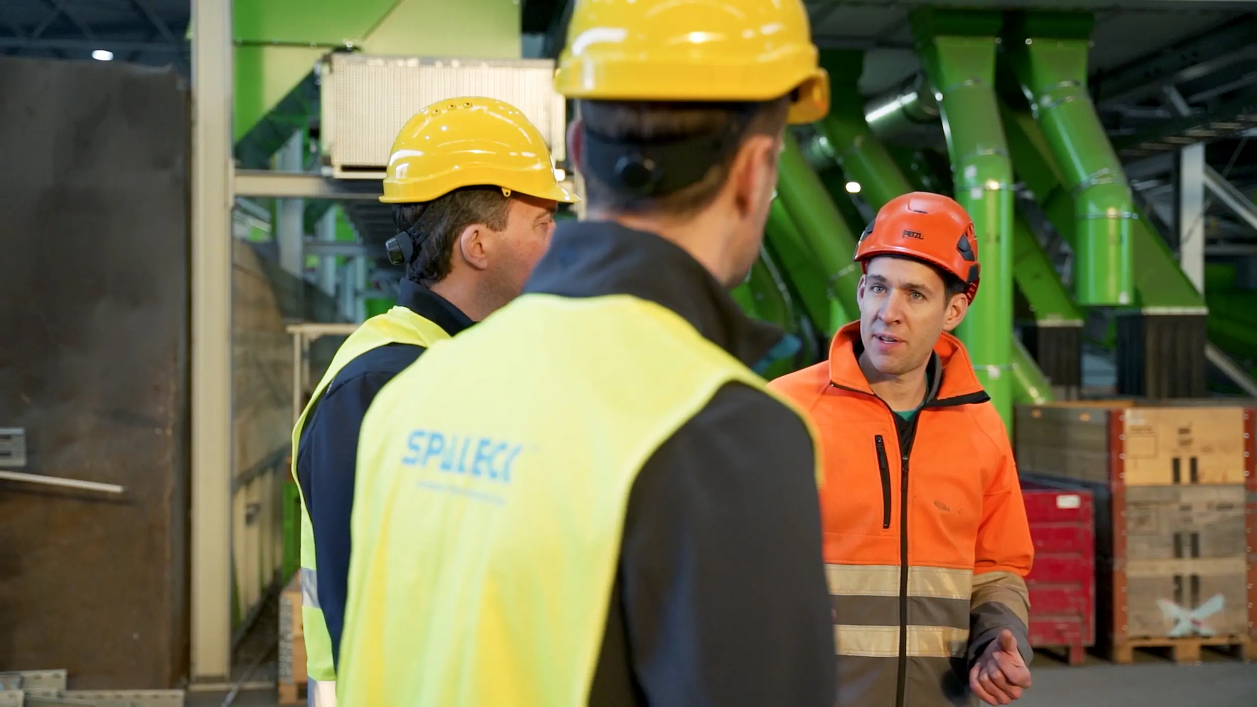 Employees wearing protective gear are discussing something at a recycling plant.
