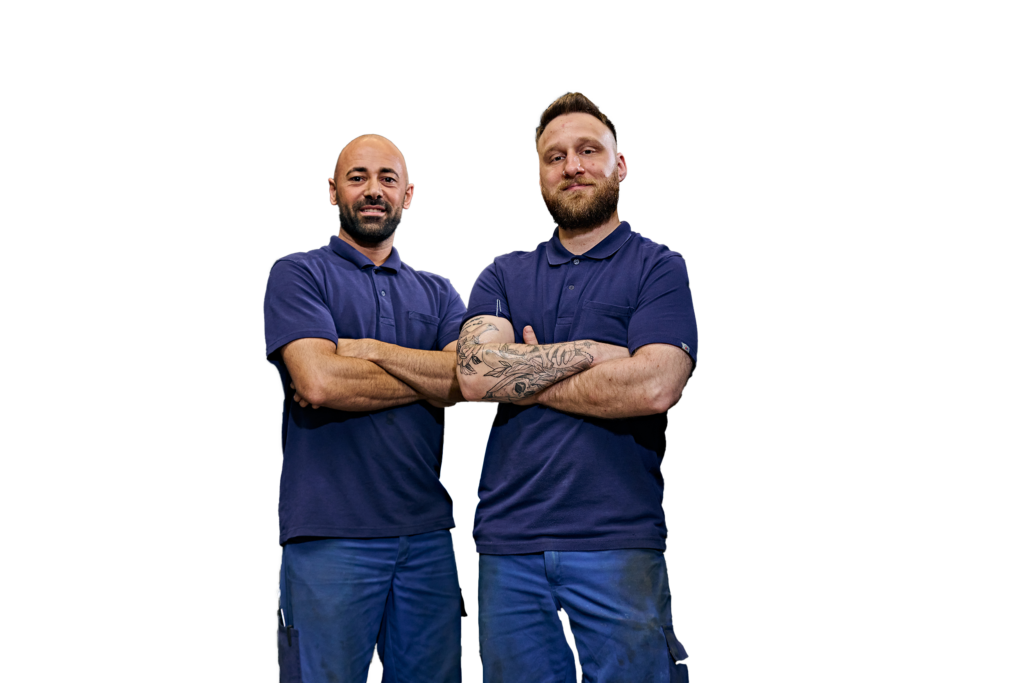Two men in work clothes stand confidently side by side.