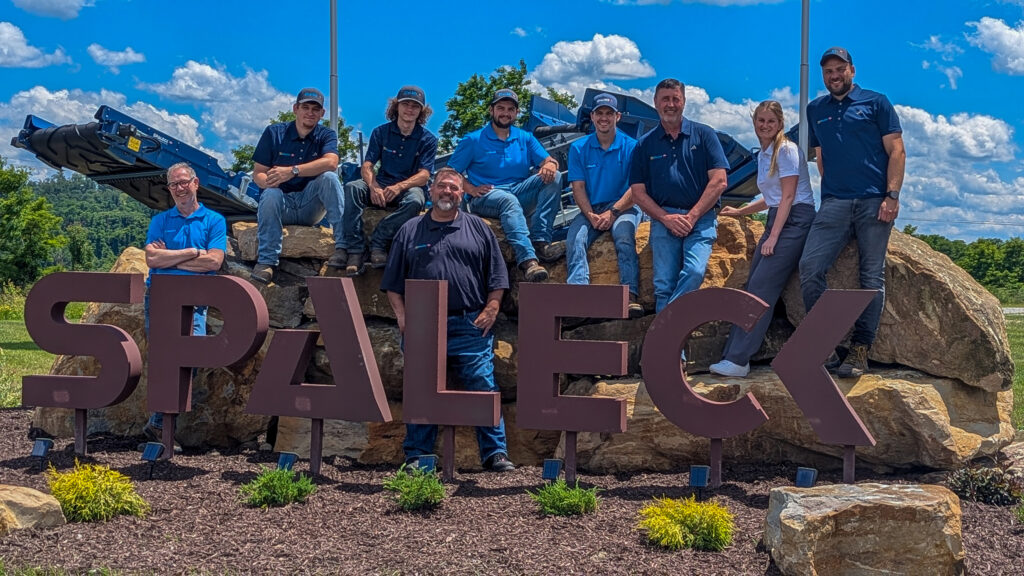 Team photo of Spaleck USA in front of the Spaleck logo in Charleroi at the site opening, with a blue sky in the background